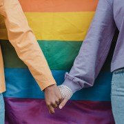 photograph of two women holding hands in front of a pride flag